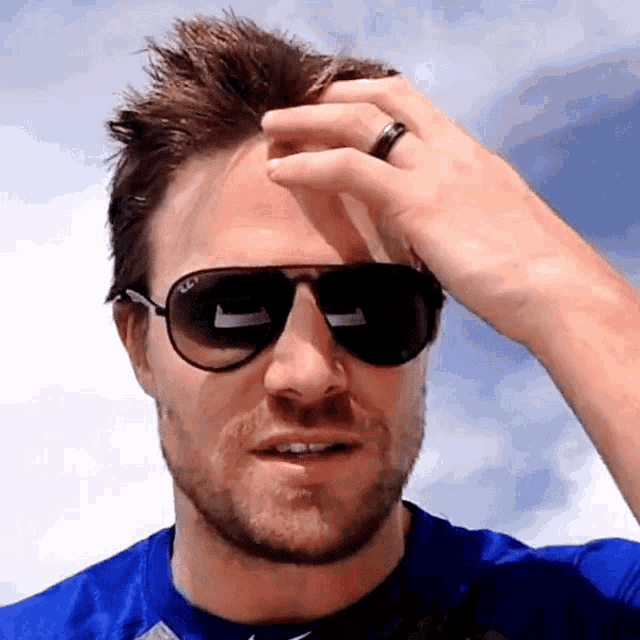 a man wearing sunglasses and a blue shirt is scratching his head