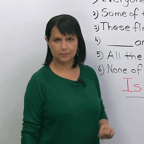 a woman in a green shirt stands in front of a white board that says some of these and all the none of is