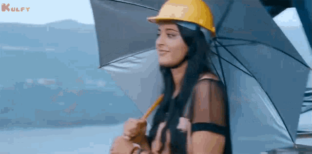 a woman wearing a hard hat and holding an umbrella is standing in the rain .