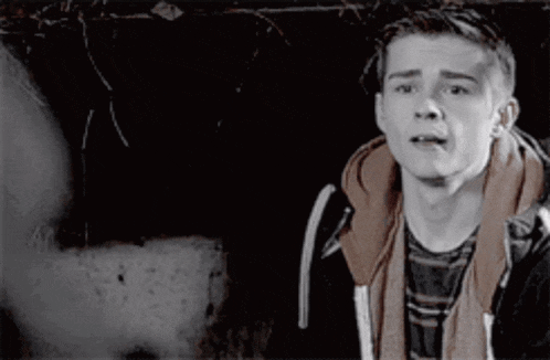 a young man in a hoodie is making a funny face while standing in a dark room .
