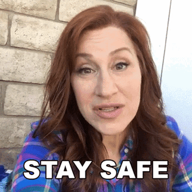 a woman wearing a plaid shirt says stay safe