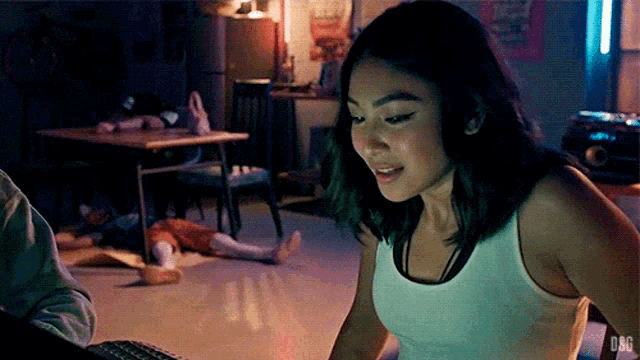 a woman in a white tank top is sitting in front of a computer keyboard with dbg written on the bottom right