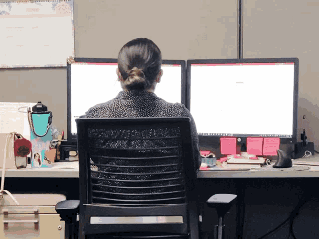 a woman sits at a desk with two computer monitors and a calendar behind her that says june