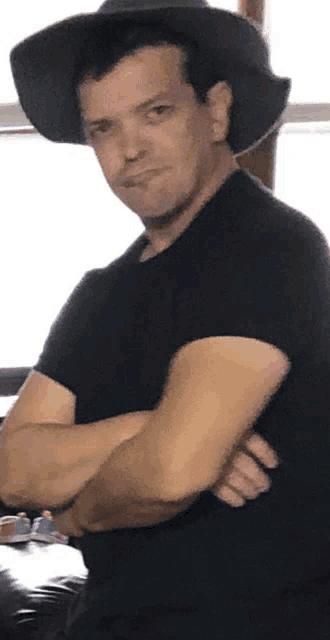 a man with his arms crossed wearing a black hat