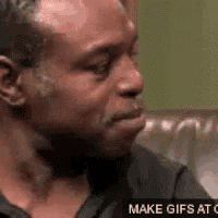 a man in a black shirt is sitting on a couch making a face .