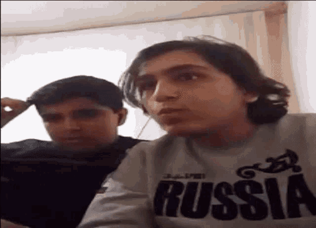 two young men are sitting next to each other in a room and one of them is wearing a russia sweatshirt .
