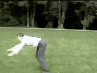 a man in a white shirt and blue pants is bending over in a field .