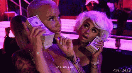 two women are holding stacks of money in front of their faces in a club .