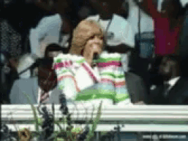 a woman singing into a microphone with a crowd behind her