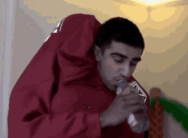 a man wearing a red jacket is drinking from a can