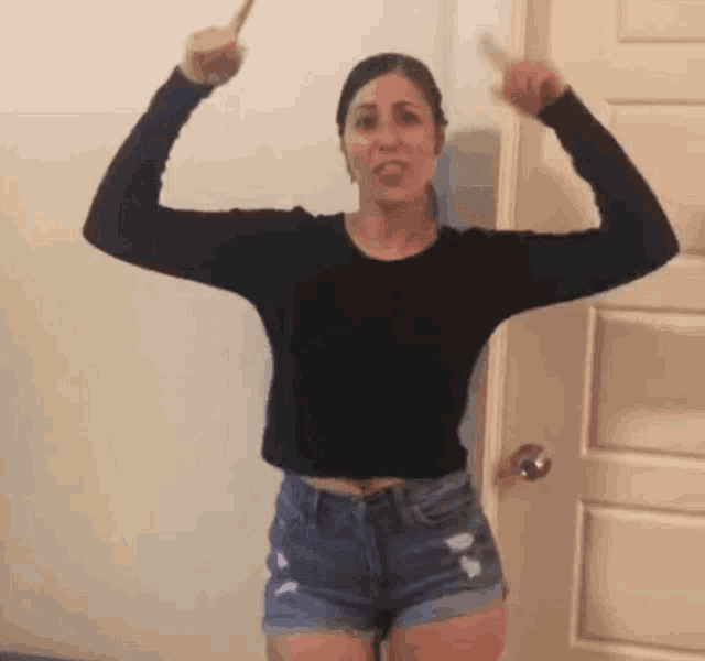 a woman in shorts and a black shirt is standing in front of a door and flexing her muscles