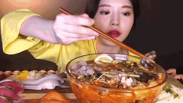a woman in a yellow shirt is eating food with chopsticks
