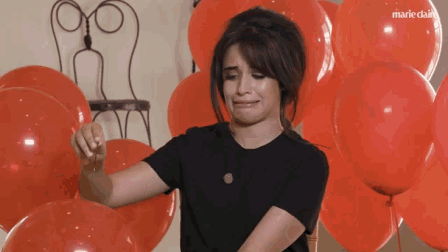 a woman in a black shirt is surrounded by red balloons with marie claire written on the bottom right