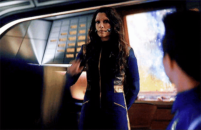 a woman in a blue and gold uniform is talking to a man
