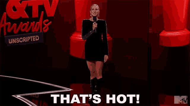 a woman stands on a stage with a microphone and the words that 's hot on the bottom
