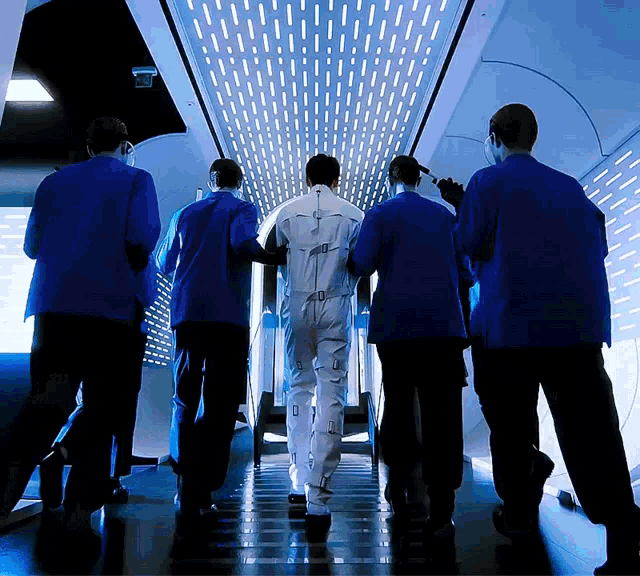 a man in a white suit is being escorted by a group of men in blue suits