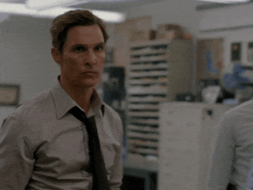 a man in a grey shirt and tie stands in a room with two other men