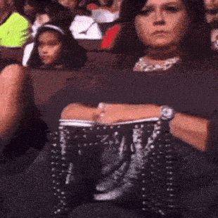 a woman is sitting in a theater holding a purse that says ' lv ' on it