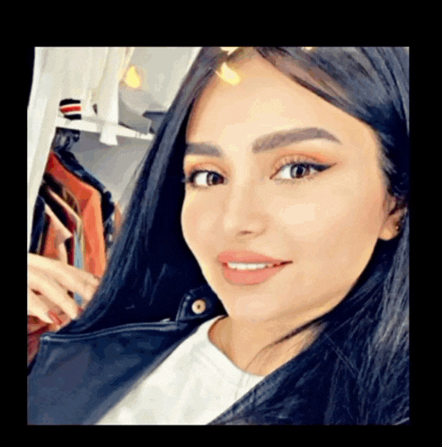 a woman with long black hair is smiling and wearing a black jacket