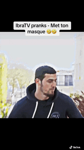a man in a black hoodie is walking down a street with a smiley face on his face .