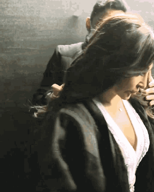 a woman in a plunging neckline top is being held by a man in a black jacket
