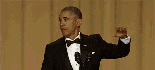 barack obama is giving a speech in front of a microphone and covering his mouth .