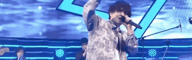 a man is singing into a microphone on a stage in front of a blue background .