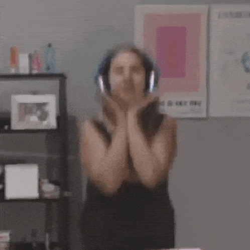 a woman wearing headphones and a black dress is dancing in a room .