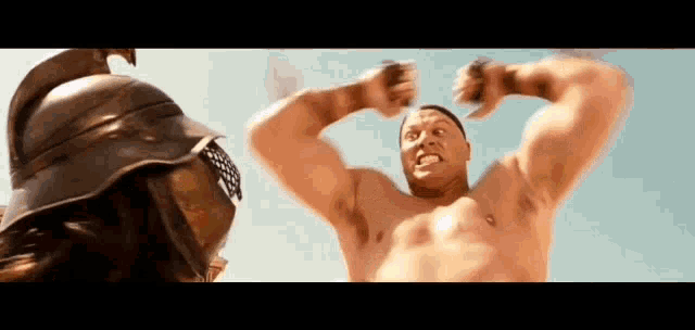 a shirtless man is flexing his muscles in front of a gladiator in a helmet .