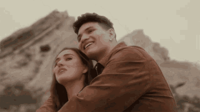 a man and a woman are standing next to each other in front of a mountain and smiling .