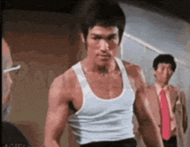 a man in a white tank top is standing in front of two men in suits and ties .