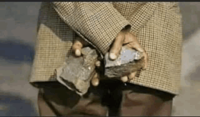 a man in a plaid jacket is holding a rock in his hands .
