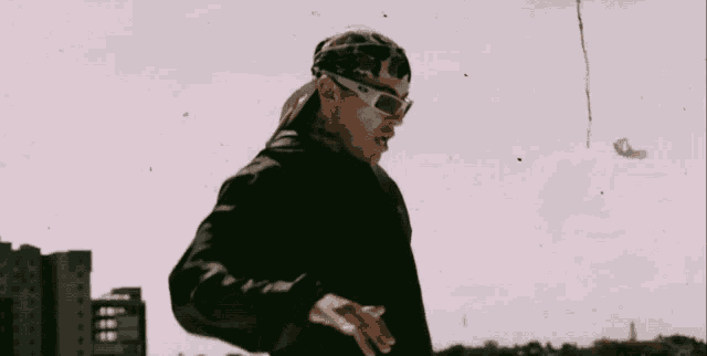 a man wearing sunglasses and a bandana stands in front of buildings