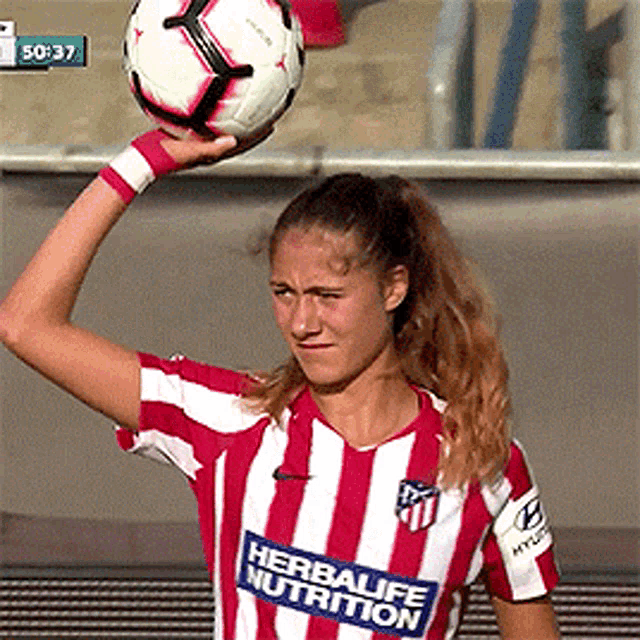 a woman in a red and white striped shirt holds a soccer ball above her head