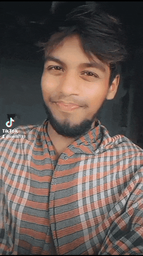 a young man in a plaid shirt is smiling for the camera with tiktok written on the bottom