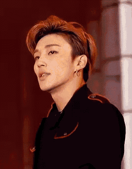 a young man wearing a black jacket and earrings is standing in front of a red wall .
