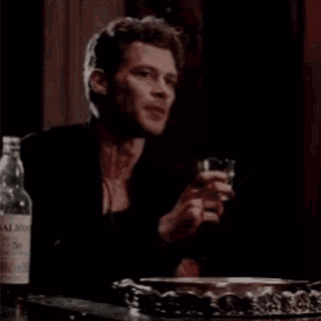a man is sitting at a table holding a glass and a bottle of alcohol .