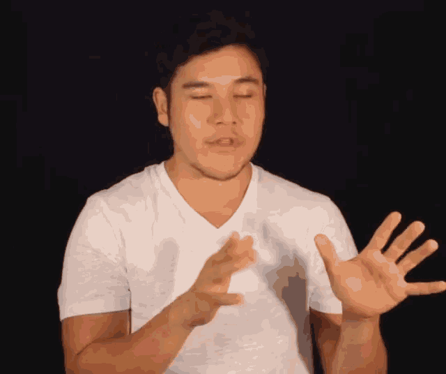 a man in a white t-shirt is making a gesture with his hands .