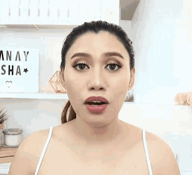 a woman is making a surprised face in front of a sign that says anay sha