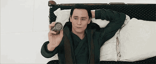 a man in a green robe is laying on a bed holding a can .
