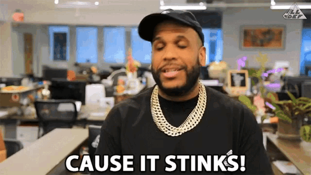 a man says cause it stinks while wearing a hat and necklace