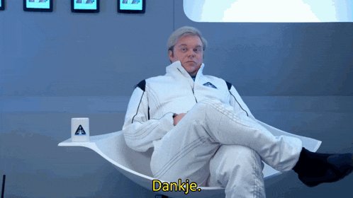 a man in a white suit sits in a chair with his legs crossed and says dankie