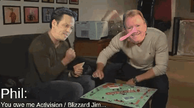 two men sit on a couch playing a game of monopoly with phil saying you owe me activision blizzard jim