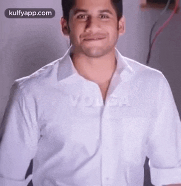 a man in a white shirt is smiling while standing in front of a wall .