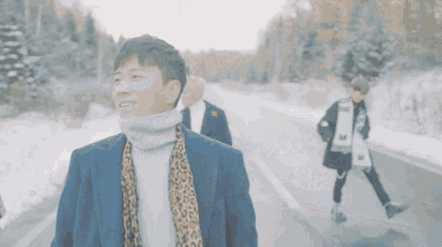 a man wearing a turtleneck and scarf walking down a snowy road