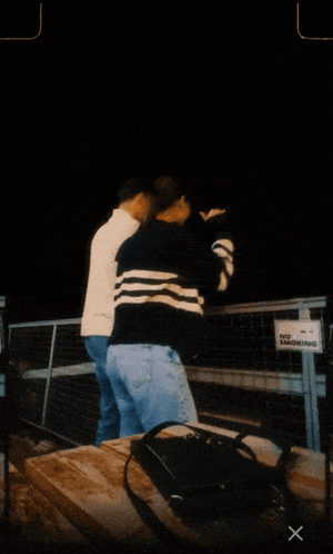 two people standing in front of a fence that has a no smoking sign on it
