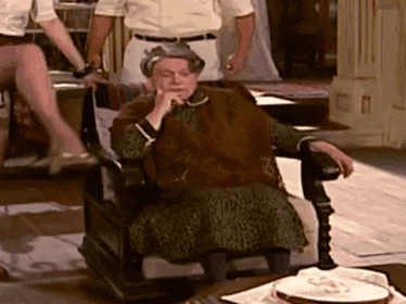 a woman sits in a chair with her hand on her chin while a man stands behind her