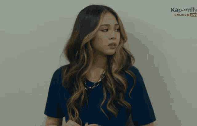 a woman in a blue shirt is standing in front of a wall that says kapamilya on it