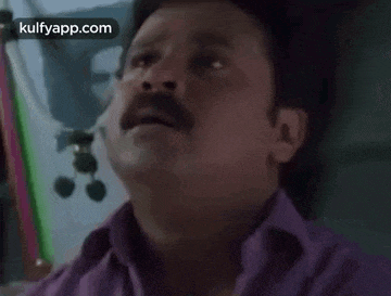 a man with a mustache is wearing a purple shirt and making a face .