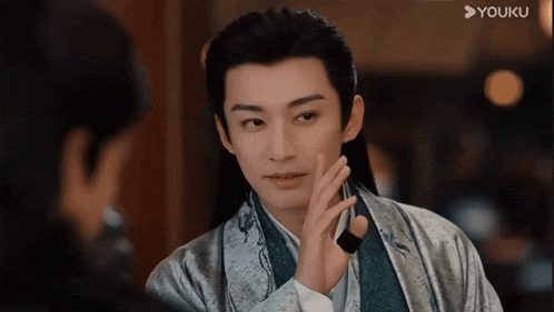 a man in a kimono is touching his face while looking at another man in a mirror .
